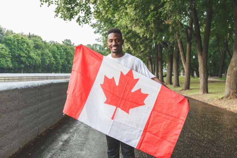 Handsome Afro American man with Canadian flag smiling at camera, standing outdoors.